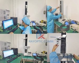 Rayoptic technician performing proof and tensile-strength tests on OptiTap flat drop cable and Fast-Connect (bayonet SC/APC) using a tensile tester alongside an insertion/return-loss meter.