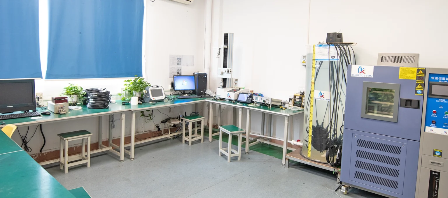 Rayoptic quality-control lab with a thermal chamber, tensile tester, water-immersion test setup, and insertion/return-loss test equipment